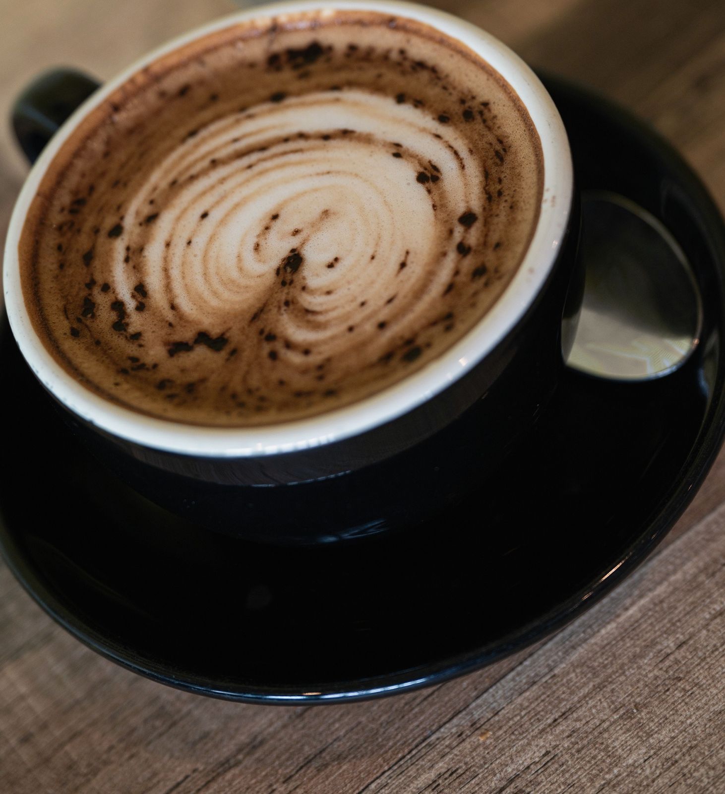 A coffee with latte art dusted with cocoa, in a black cup on a timber table