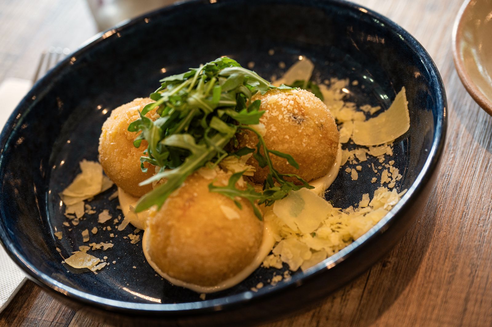 Arancini on rocket with shaved parmesan in a dark blue bowl