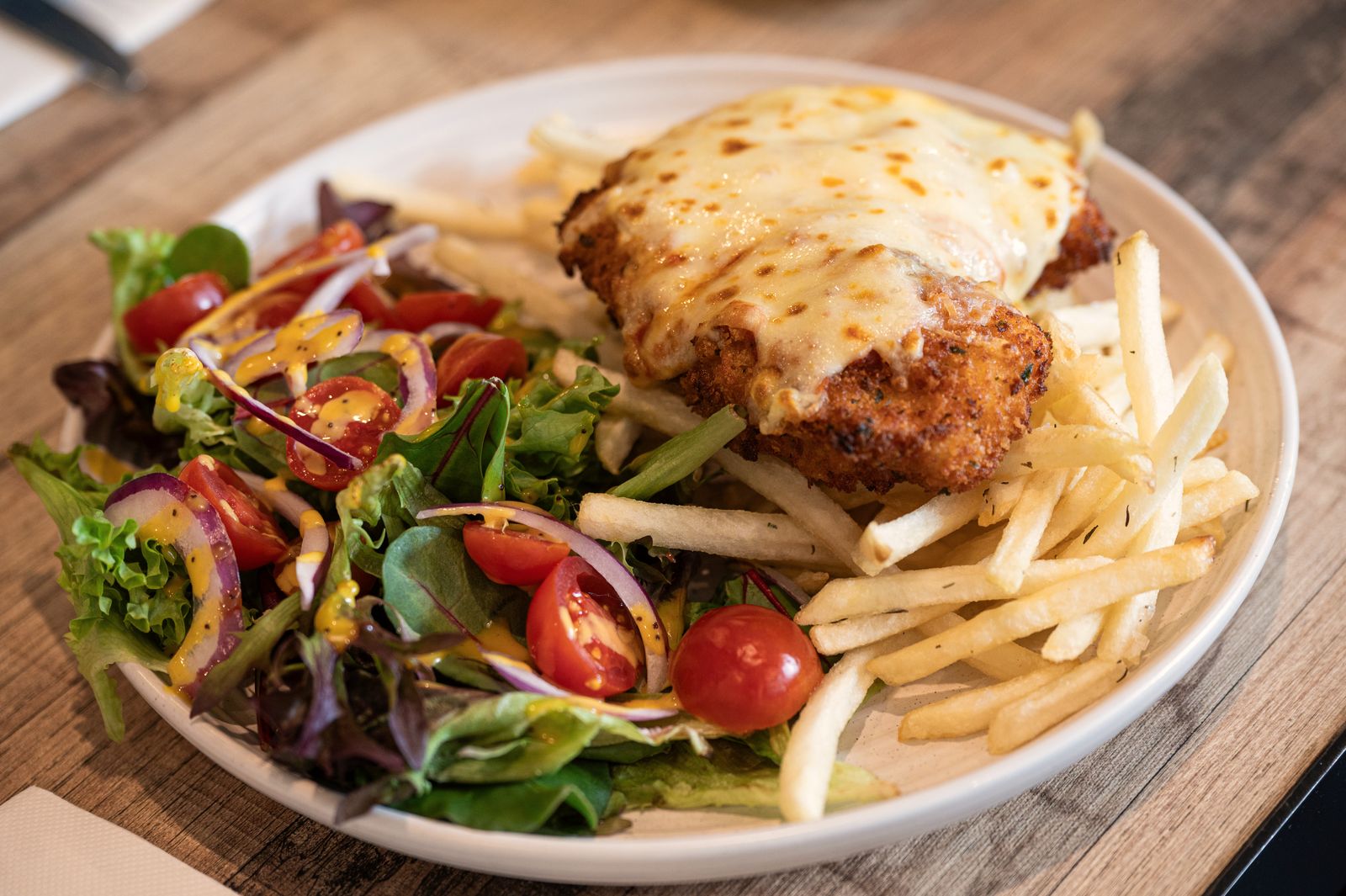 Chicken parmigiana with chips and a garden salad on a white plate