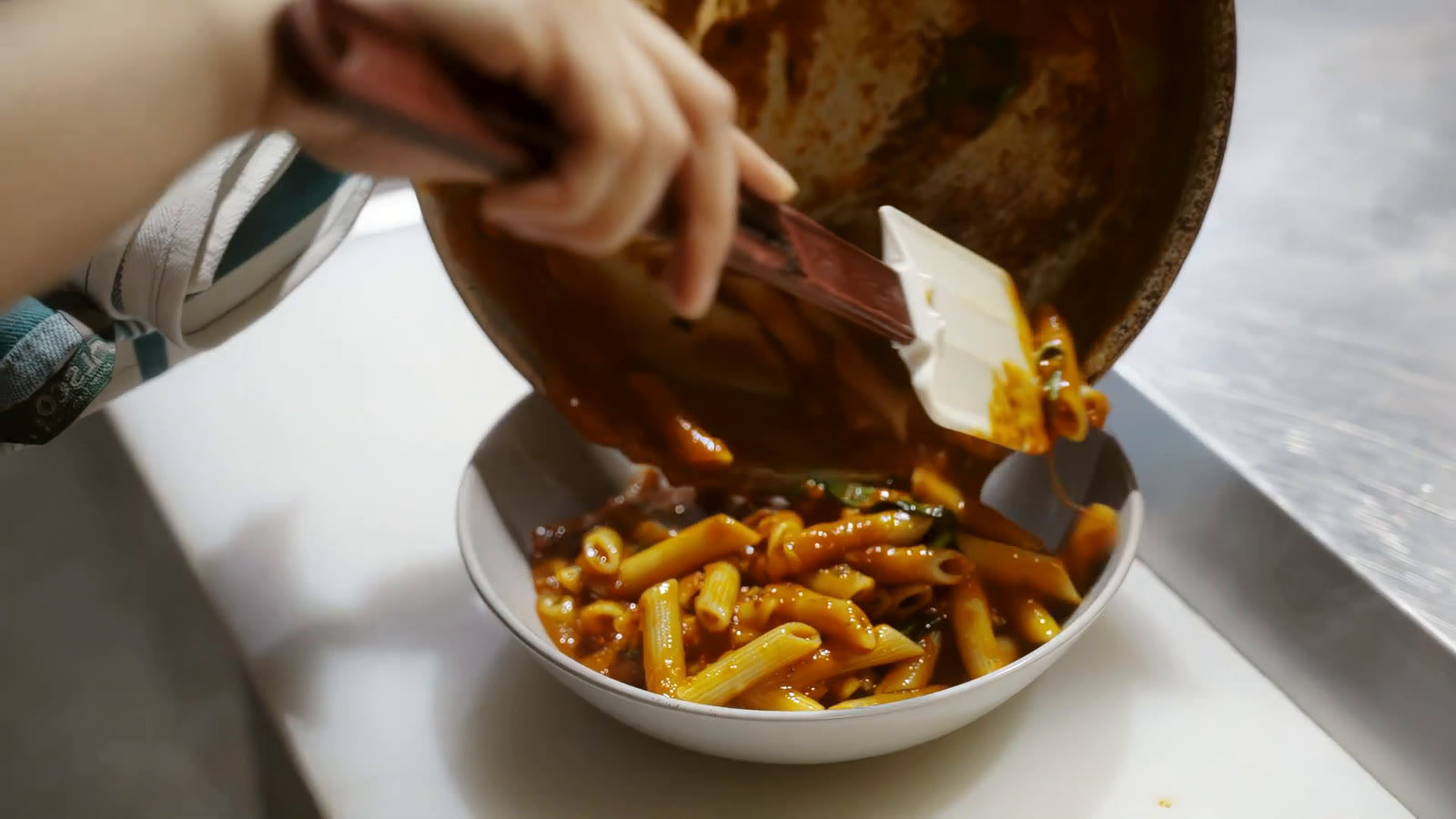 Pasta going from the pan into a white bowl in the Glenunga kitchen