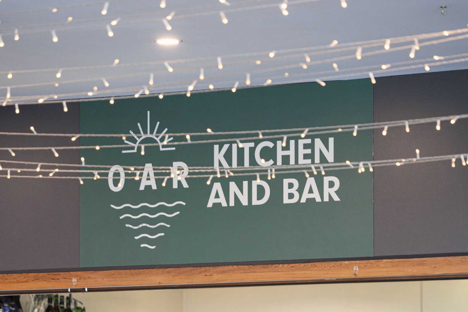 The green Oar Kitchen and Bar sign over the counter at Glenunga, under strings of festoon lights